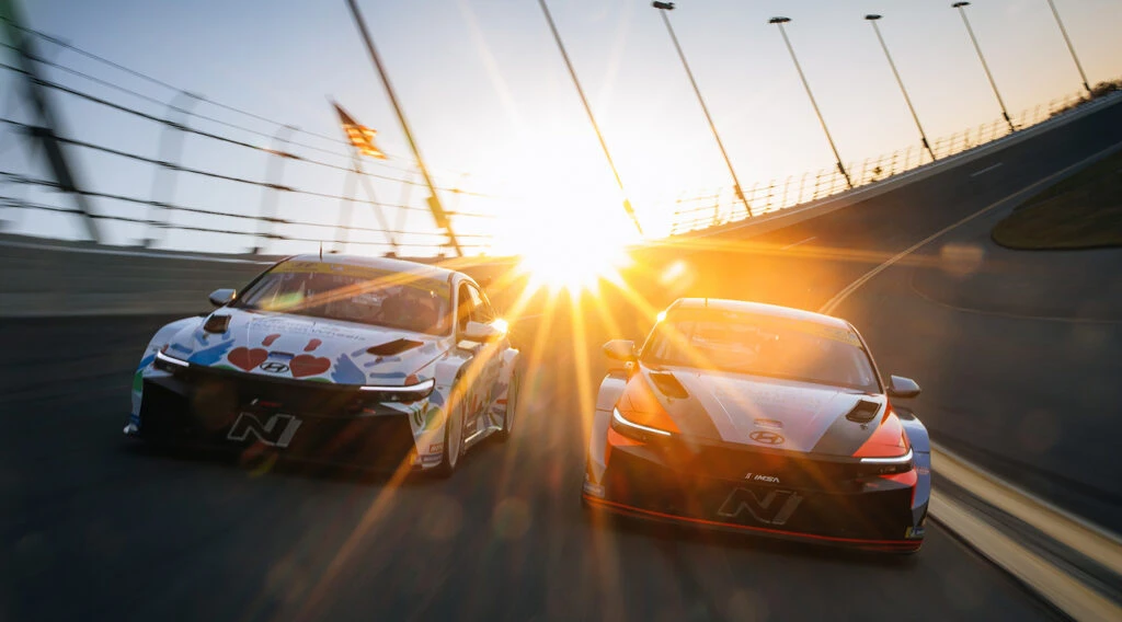 Two Hyundai N TCR race cars on a banked oval at sunset