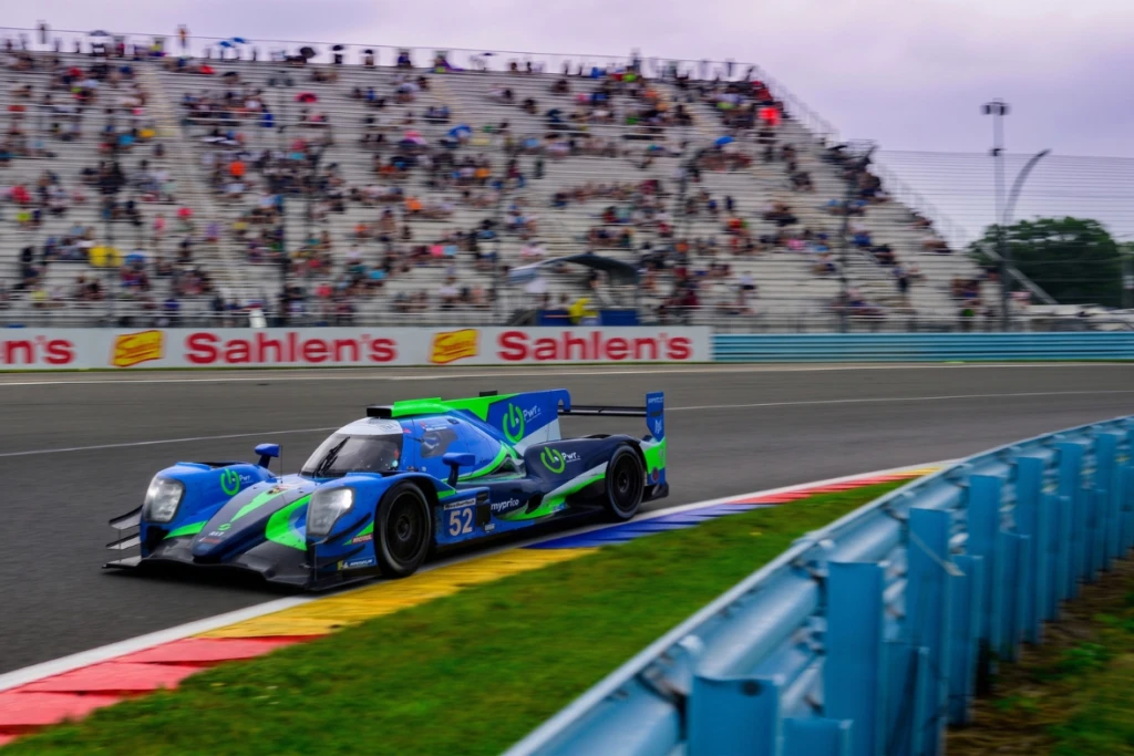 A blue and green IMSA prototype at speed past the grandstands at Watkins Glen